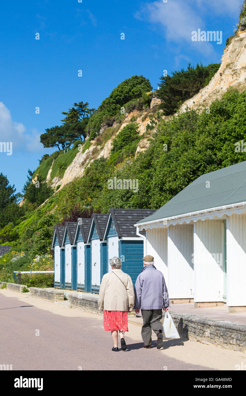 Couple de personnes âgées à marcher le long des cabines de plage promenade à Poole, Dorset en Juillet Banque D'Images