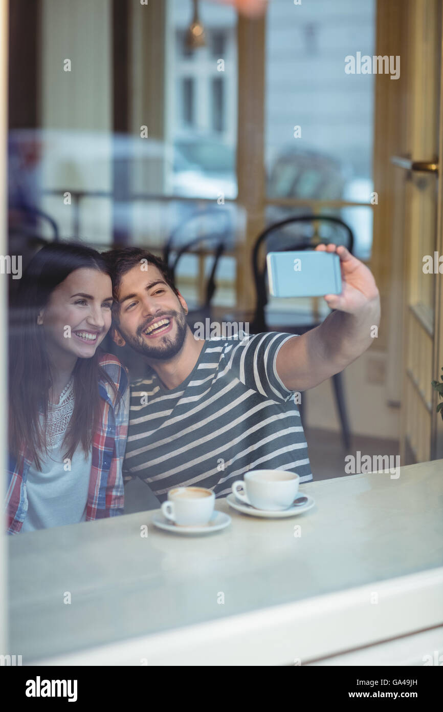 Cheerful couple en tenant au café selfies Banque D'Images