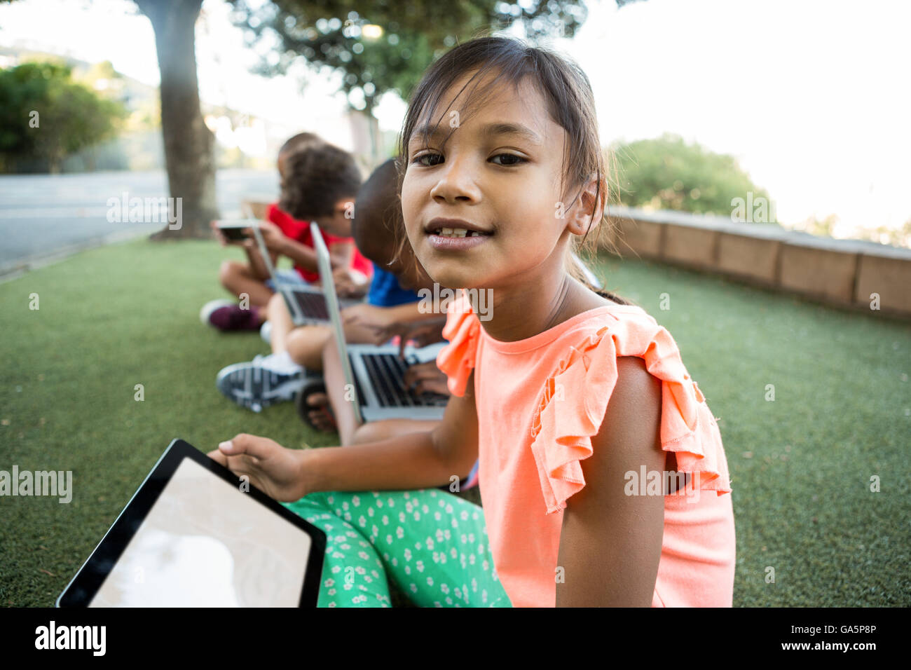 Fille avec des amis à l'aide de digital tablet at park Banque D'Images