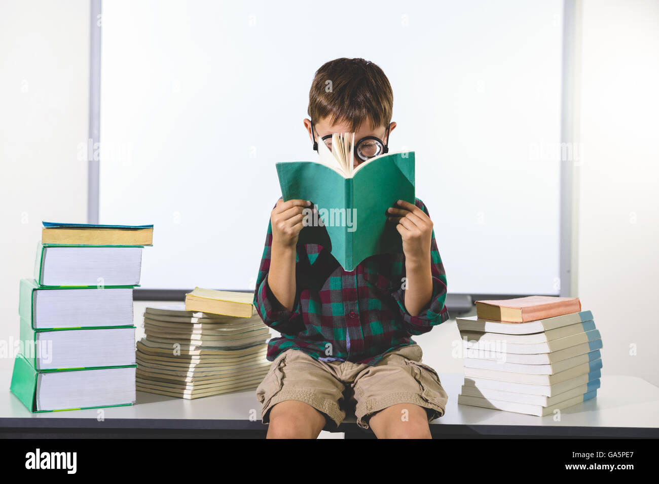 Elementary boy reading book while sitting in classroom Banque D'Images