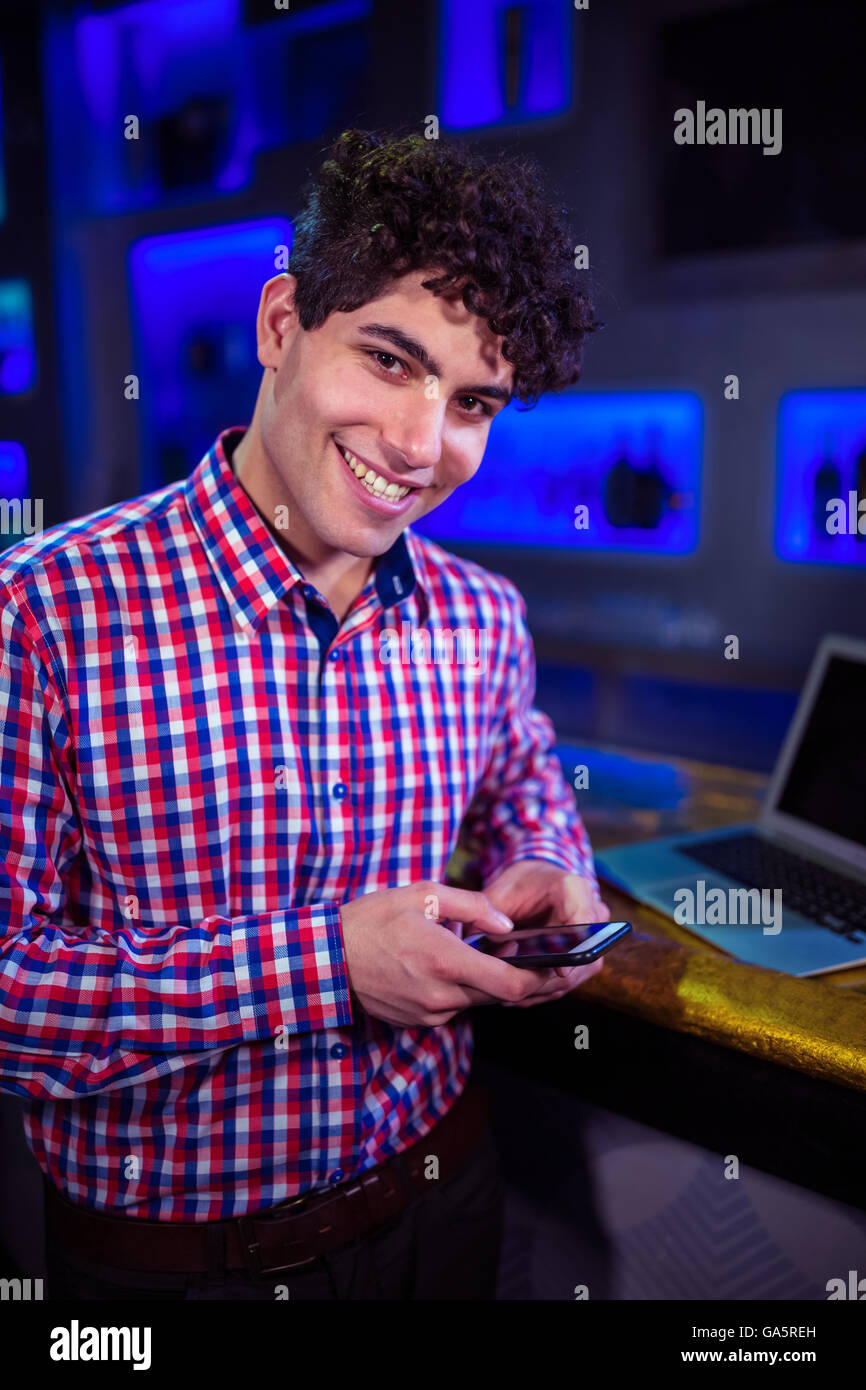 Portrait of smiling man holding mobile phone par comptoir bar Banque D'Images