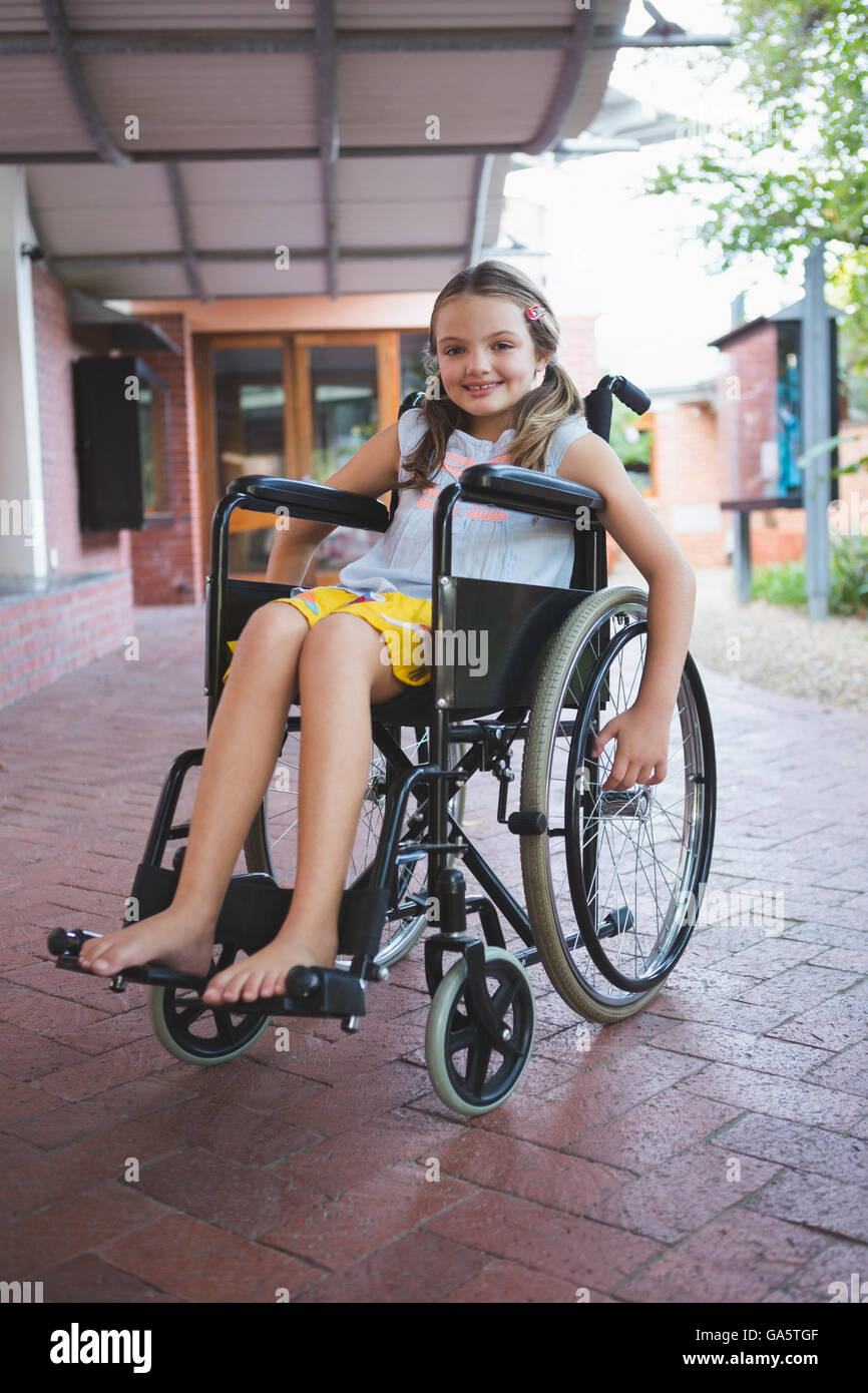 Portrait of cute girl sitting on wheelchair in corridor Banque D'Images