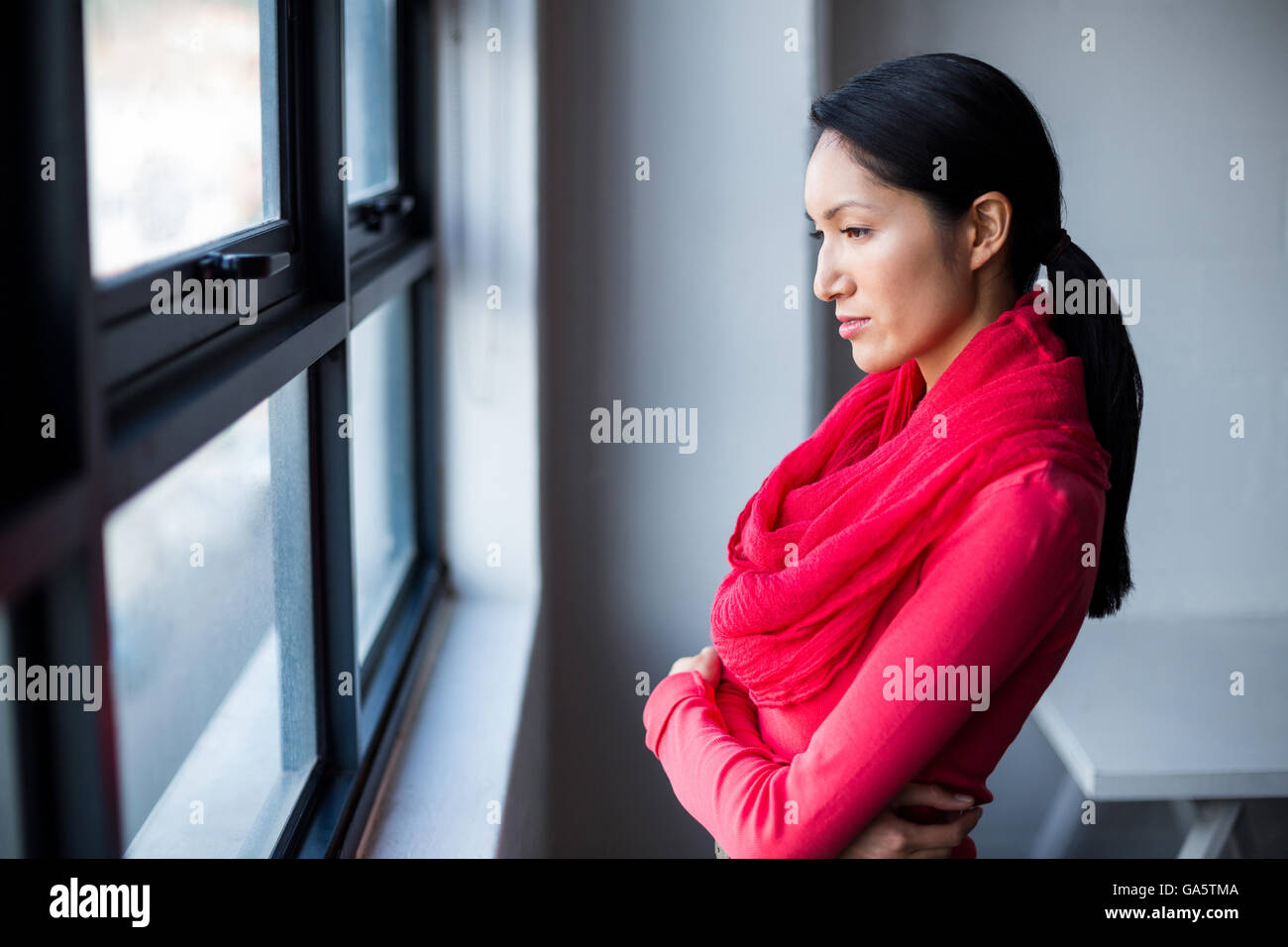 Thoughtful woman standing by window in office Banque D'Images