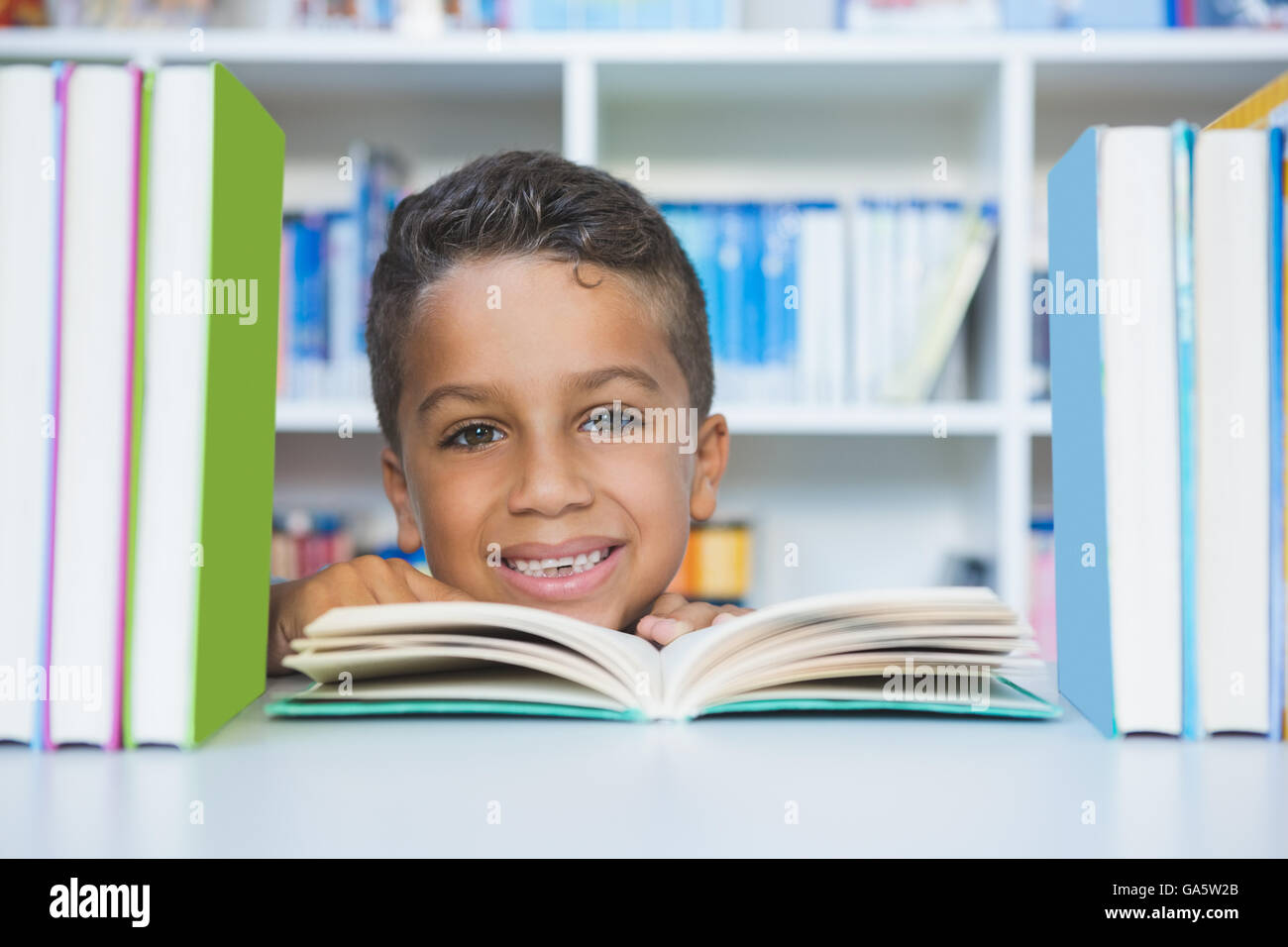 Écolier assis sur table et reading book in library Banque D'Images