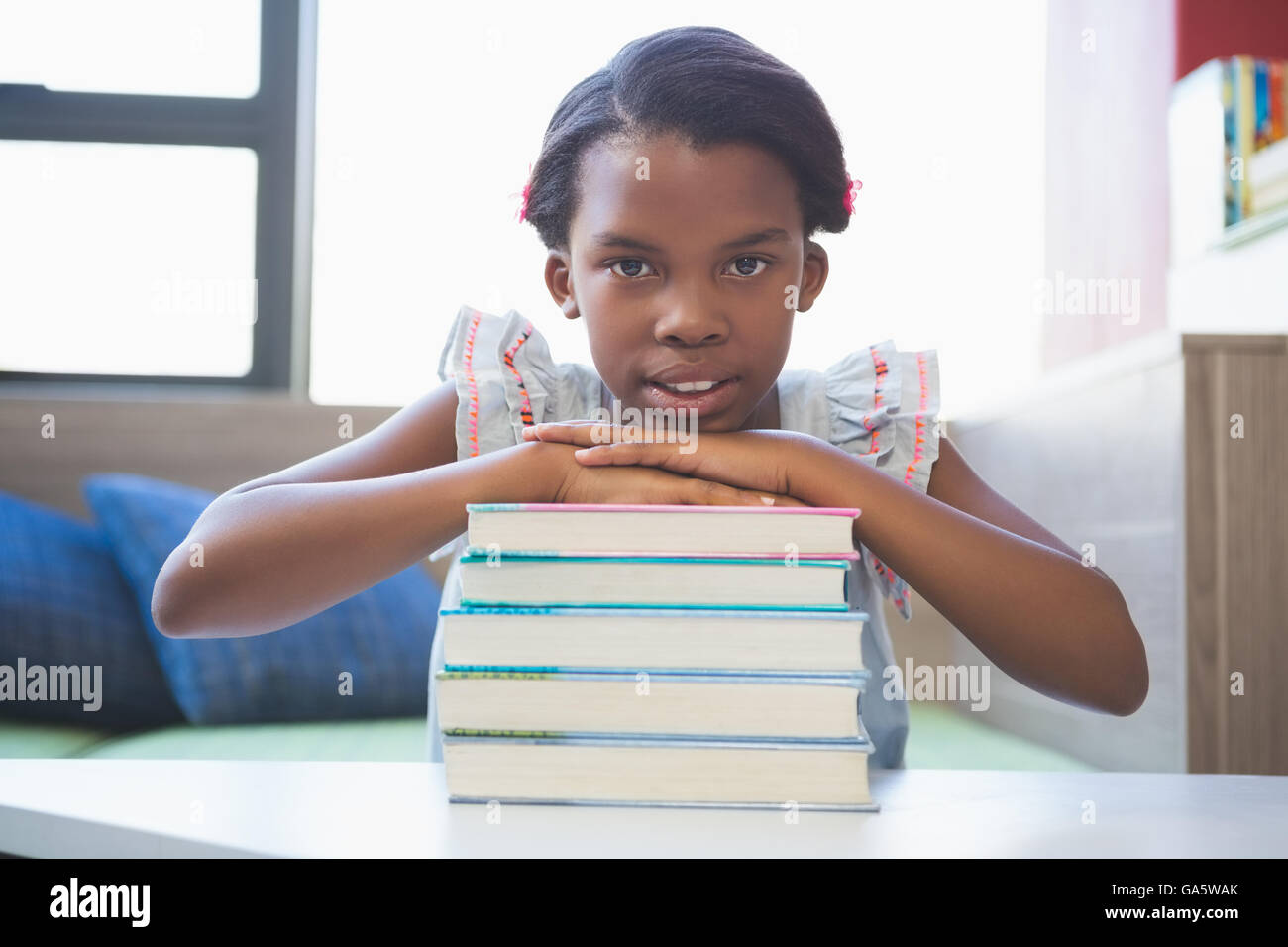Portrait of smiling girl leaning on pile de livres dans la salle de classe Banque D'Images