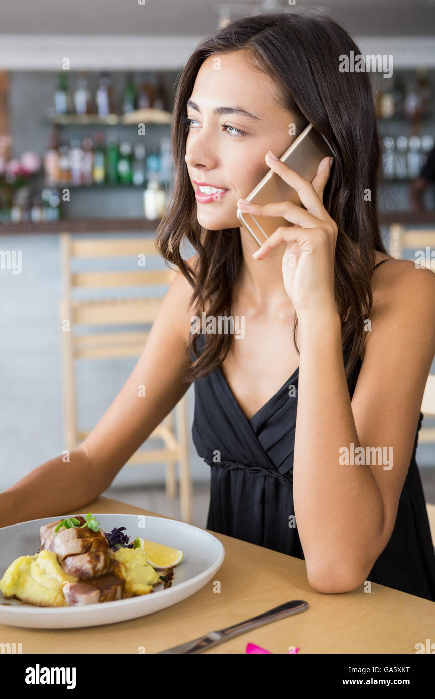 Woman talking on mobile phone while having meal Banque D'Images