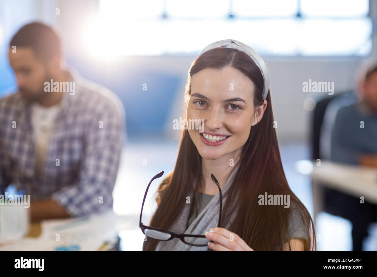 Smiling businesswoman holding eyeglasses at office Banque D'Images