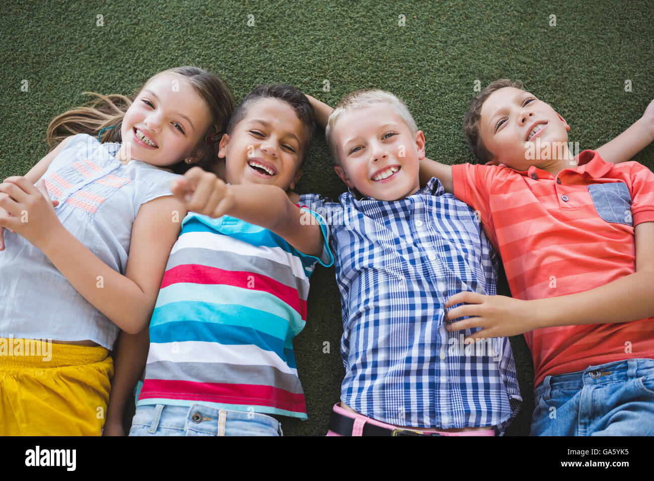 Smiling schoolkids lying on grass in campus Banque D'Images