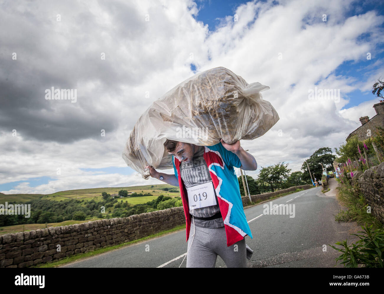 Un concurrent prend part à la ferme de la course de la paille dans le Yorkshire, qui consiste à courir en robe de soirée, tout en portant une botte de paille et se rendant sur chacune des pubs locaux dans le village pour récolter des fonds pour des œuvres de bienfaisance. Banque D'Images