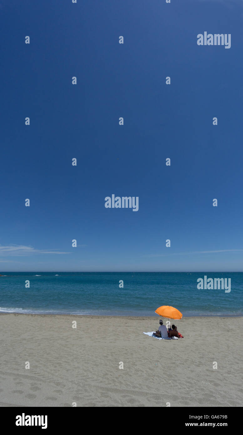Les baigneurs solitaires sous un parasol sur une plage d'orange Banque D'Images