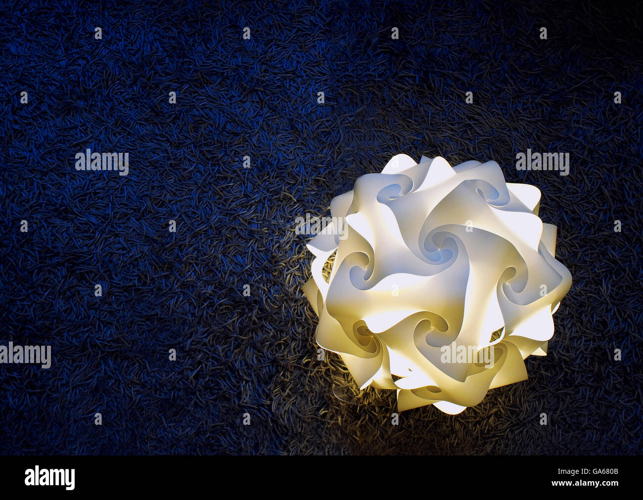 Une lampe intérieure, dans la forme d'une fleur, qu'il est allumé et placé sur un tapis bleu foncé. La composition minimaliste. Banque D'Images