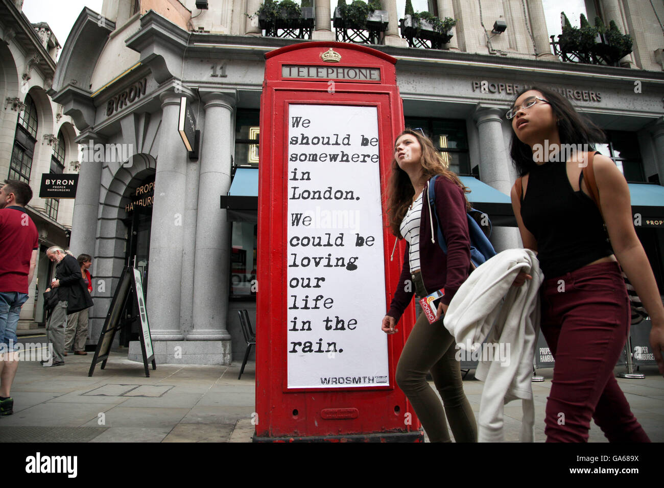 Les femmes passent par un devis pour une cabine téléphonique rouge sur Haymarket, dans le centre de Londres. Banque D'Images