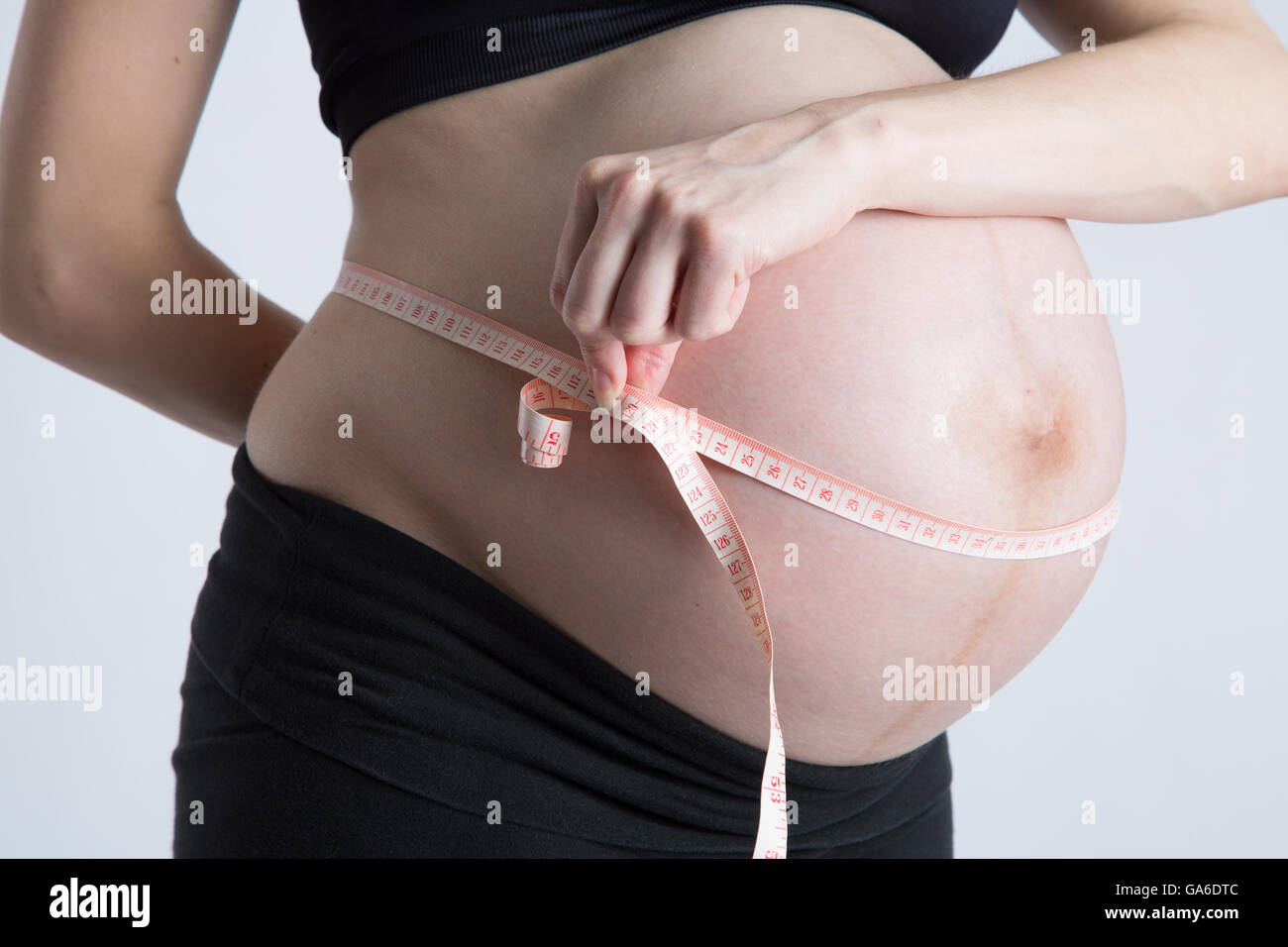 Une femme enceinte est titulaire d'un ruban à mesurer autour de son ventre enceinte. Banque D'Images