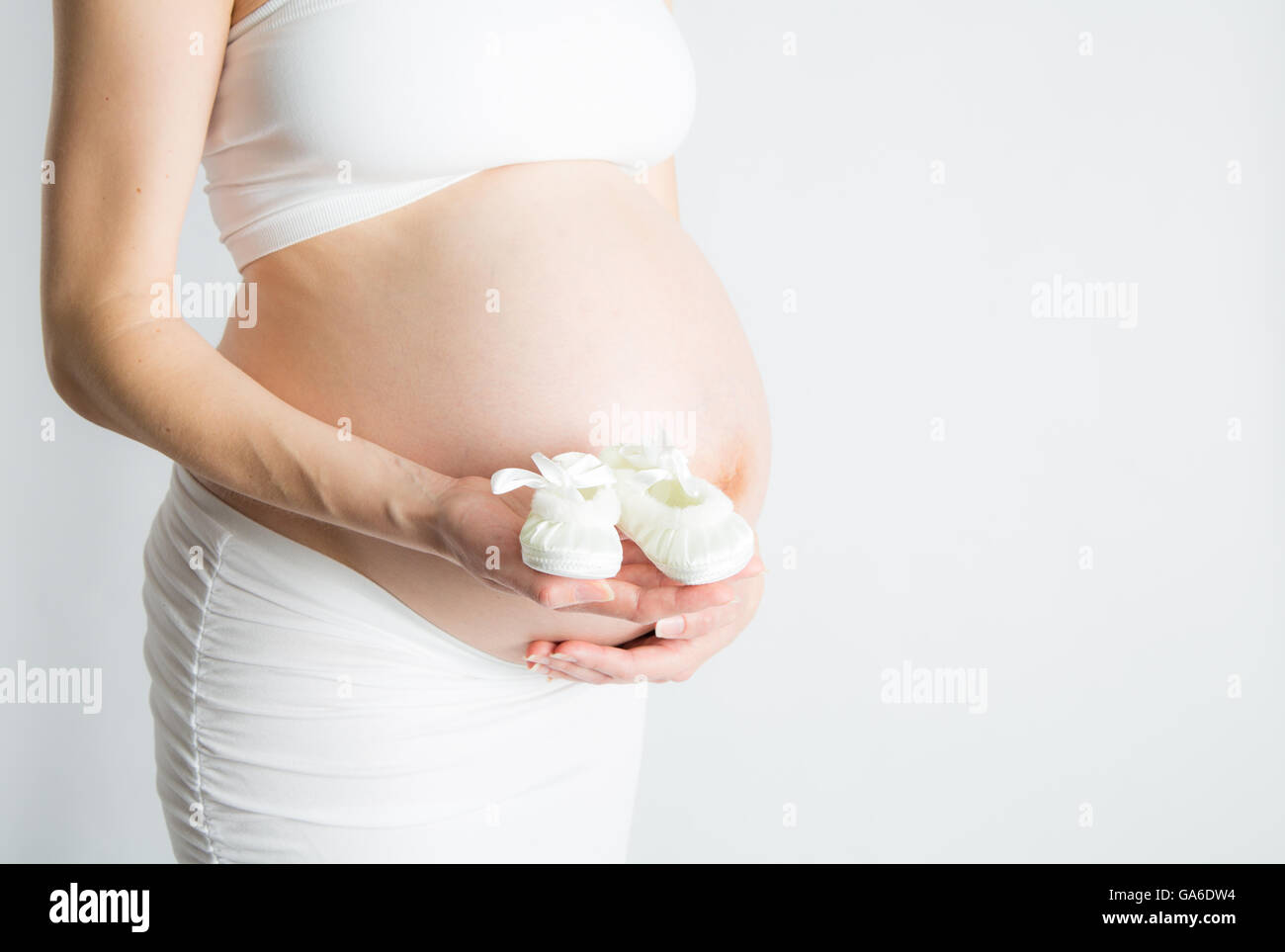 Une femme enceinte est titulaire d'une paire de chaussures de bébé en face de son ventre enceinte. Banque D'Images