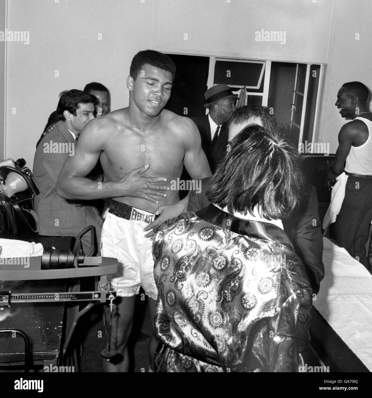 Le champion du monde de poids lourd Muhammad Ali (Cassius Clay) sourit que Lord Sutch (de retour à la caméra) est intégré à son dressing. Le chanteur de pop devait participer à une séance d'entraînement, mais après s'être mis en retard, il a éclaté dans le dressing du champion pour le frapper dans l'estomac. Banque D'Images