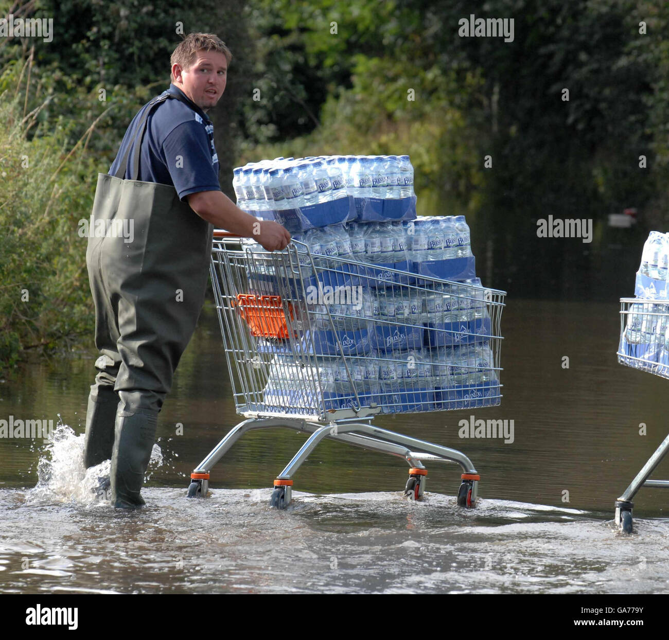 Des tempêtes ont frappé le Royaume-Uni.Un homme pousse un trolley d'eau embouteillée dans les eaux d'inondation de Sandhurst, près de Gloucester. Banque D'Images