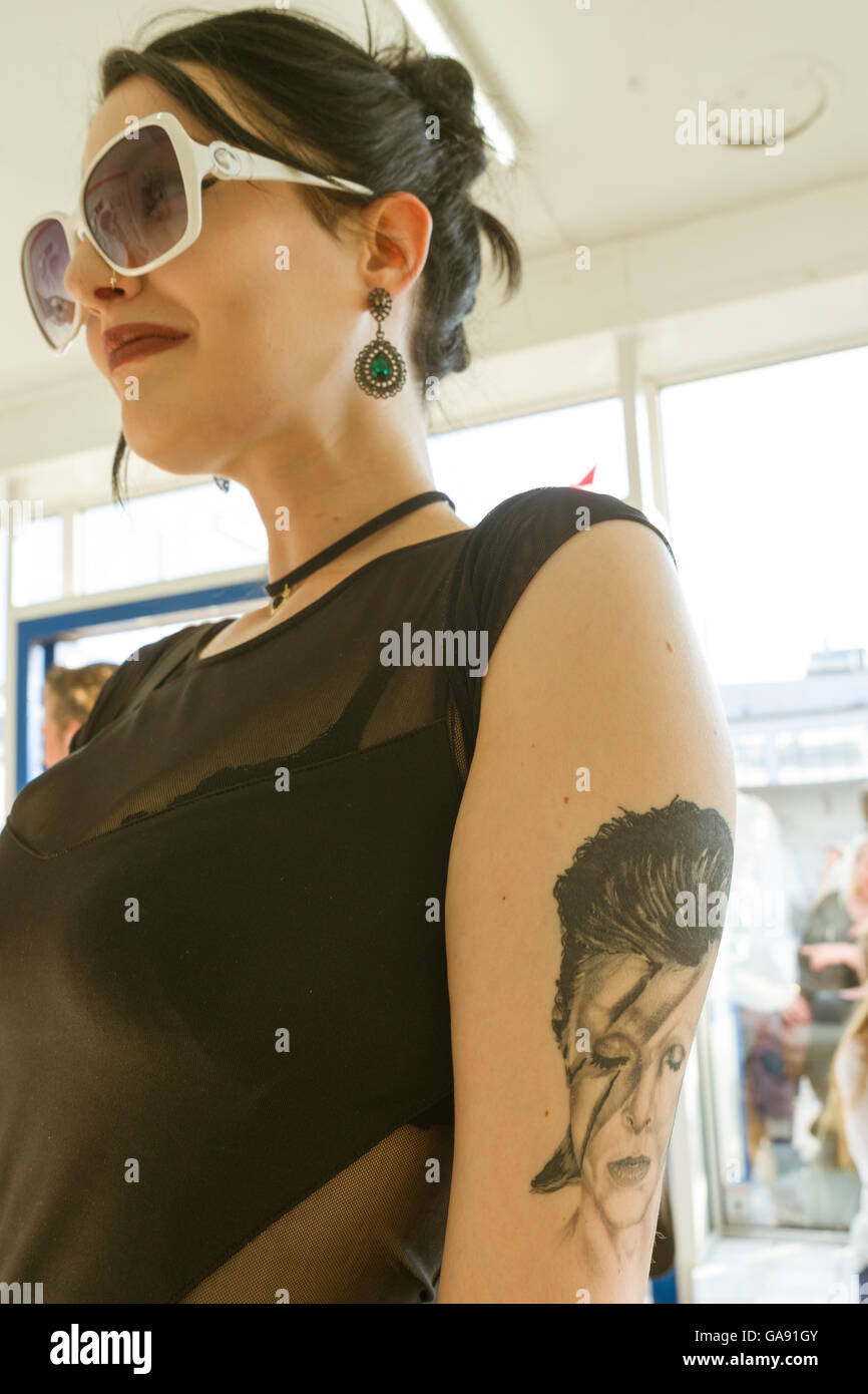 Jeune femme avec tatouage de David Bowie sur son bras portant des lunettes blanches Banque D'Images
