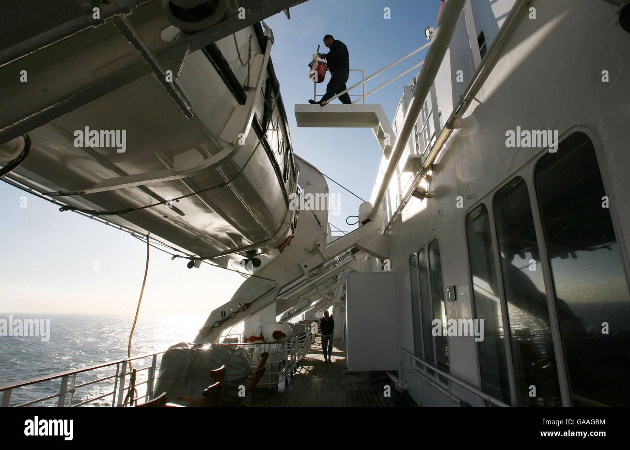Un membre de l'équipage à bord du QE2 donne à un canot de sauvetage une nouvelle couche de peinture alors qu'elle navigue à Newcastle depuis Southampton lors de sa croisière du 40e anniversaire autour de la Grande-Bretagne. Banque D'Images