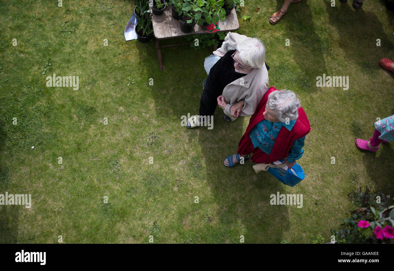 Deux femmes âgées à pied dans les bras tout en faisant des emplettes pour les plantes lors d'une fête du village de Morth Matravers, Dorset, Angleterre, Banque D'Images