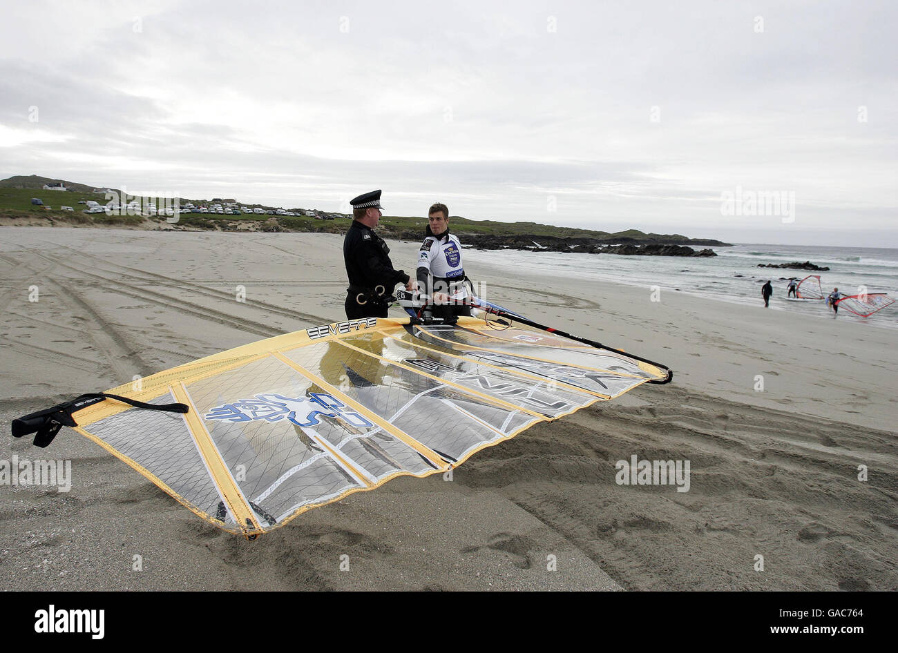 Le policier local Danny Lapsley de la police de Strathclyde, qui est le seul officier sur l'île de Tiree, parle avec le windsurfeur finlandais Tuomo Naalisvaara pendant son battement sur la plage de Balevullin sur l'île de Tiree. Banque D'Images