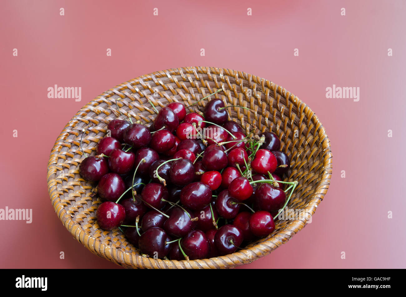 Cerise rouge avec des tiges vertes en panier tressé Banque D'Images