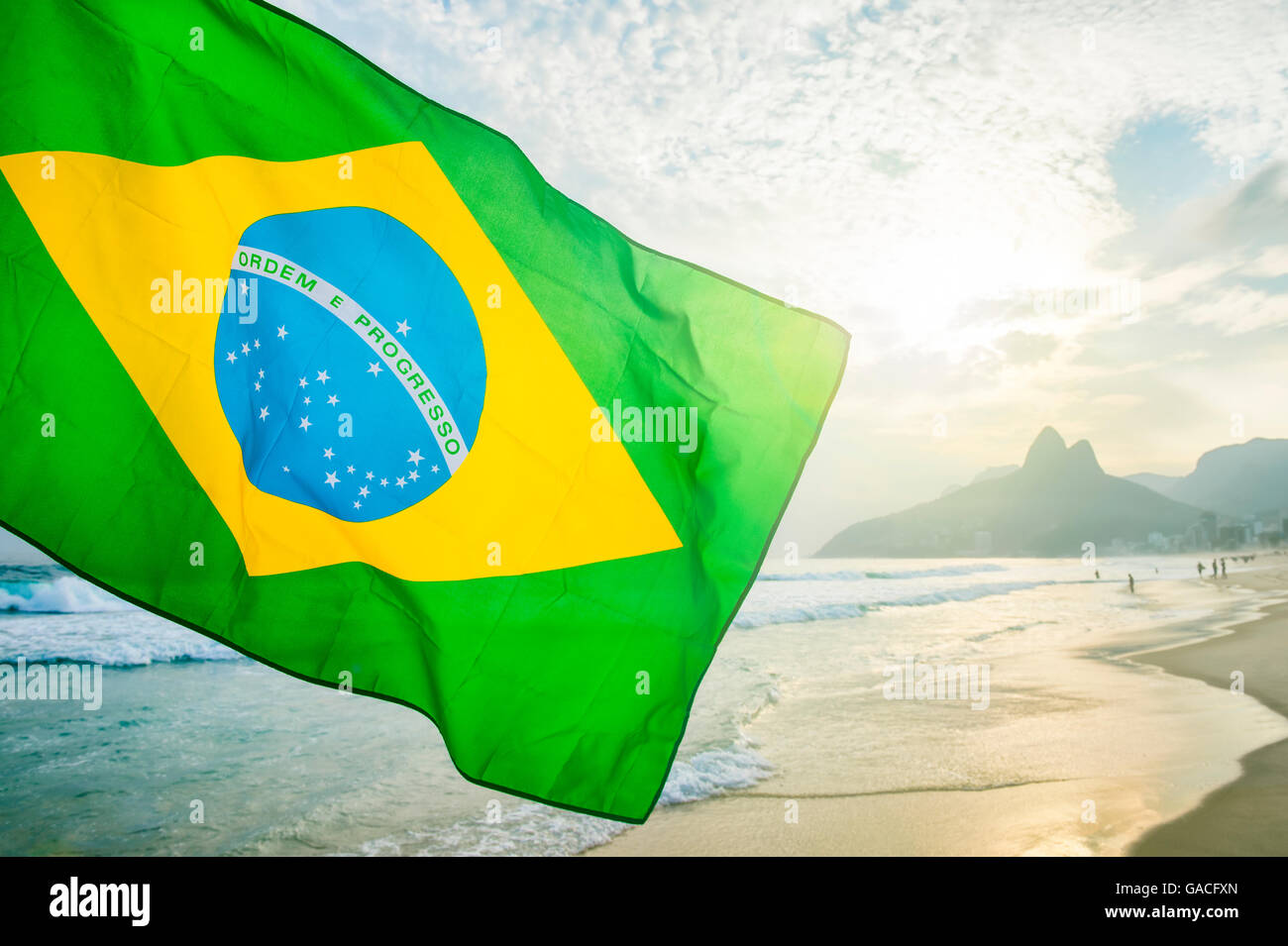 Brandir le drapeau brésilien en face de l'horizon le coucher du soleil à la plage d'Ipanema à Rio de Janeiro, Brésil Banque D'Images
