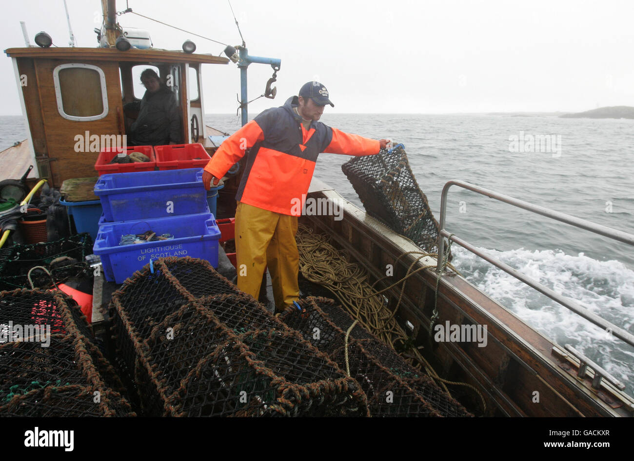 Pêcheur de homard Ross MacLennon Skipper du bateau « Carrie Anne » De Milton Harbour sur l'île de Tiree avec matelet William Walker (portant un chapeau) Jeter des pots de homard à la mer alors qu'ils atterrtent du homard dans le Océan Atlantique Banque D'Images