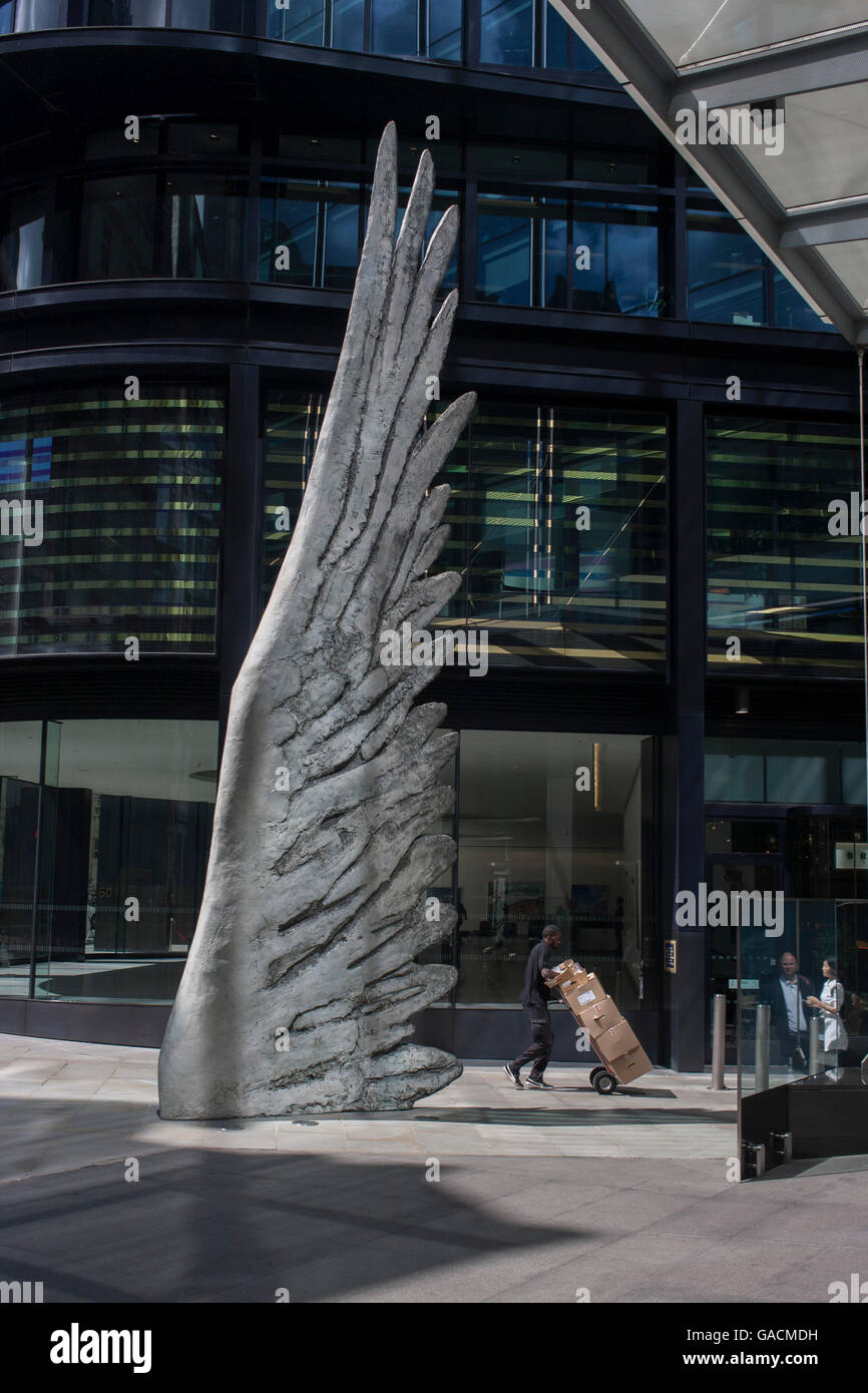 Les travailleurs de la ville par le passage de l'oeuvre d'un géant de l'aile de bronze lors d'un midi de printemps dans le quartier financier de Londres, le 4 juillet, Londres, Royaume-Uni. Comme la lumière se reflète sur les immeubles de bureaux à proximité, la foule à l'heure du déjeuner devant ce géant des illustrations sur leur façon de réunions et sandwicheries. Les dix mètres de haut est la sculpture en bronze par le président de la Royal Academy of Arts, Christopher Le Brun, commandé par Hammerson en 2009. Elle est appelée 'La Ville' de l'aile et a été jeté par Morris Singer, fondateurs de l'art réputé pour être la plus ancienne fonderie d'art dans le monde. Banque D'Images