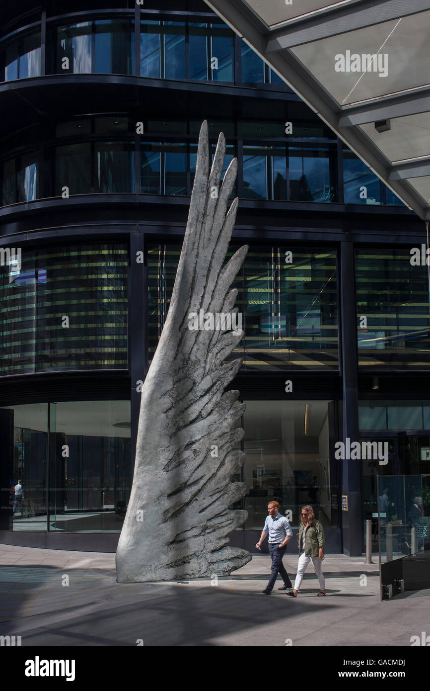 Les travailleurs de la ville par le passage de l'oeuvre d'un géant de l'aile de bronze lors d'un midi de printemps dans le quartier financier de Londres, le 4 juillet, Londres, Royaume-Uni. Comme la lumière se reflète sur les immeubles de bureaux à proximité, la foule à l'heure du déjeuner devant ce géant des illustrations sur leur façon de réunions et sandwicheries. Les dix mètres de haut est la sculpture en bronze par le président de la Royal Academy of Arts, Christopher Le Brun, commandé par Hammerson en 2009. Elle est appelée 'La Ville' de l'aile et a été jeté par Morris Singer, fondateurs de l'art réputé pour être la plus ancienne fonderie d'art dans le monde. Banque D'Images