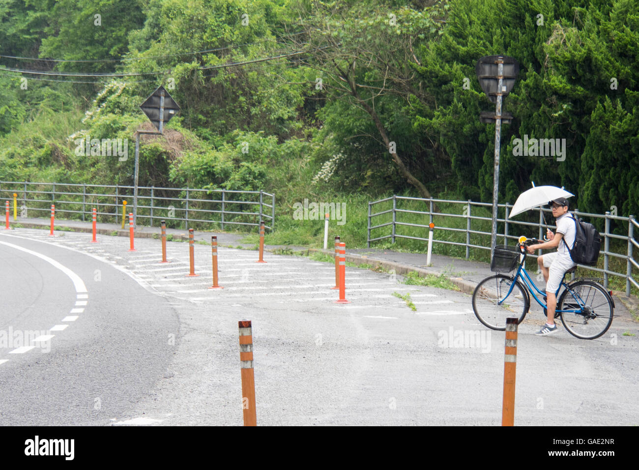 Un jeune homme japonais d'une bicyclette tout en tenant un parapluie. Banque D'Images