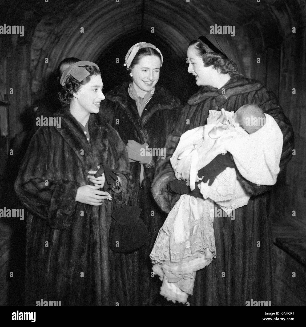 Tandis que le centre d'attraction, le bébé Alexander Peppys Muir, des slumbers dans les bras de sa mère, Lady Rosemary Muir, sa marraine royale, la princesse Margaret, regarde vers le bas souriant sur lui dans le porche de l'église de Woodstock, Oxfordshire, où il a été baptisé cet après-midi. L'enfant est le petit-fils du duc et de la duchesse de Marlborough. Son père est M. Robin Muir. Banque D'Images