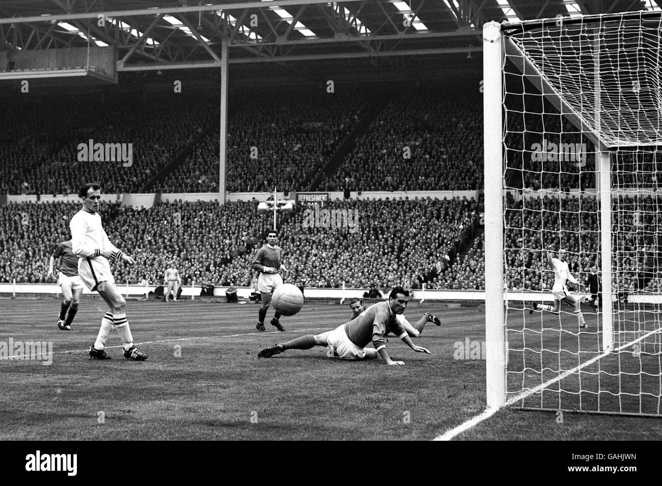 Football - FA Cup - finale - Manchester United / Leicester City.Noel Cantwell de Manchester United (c, sur le sol) observe la mouche de balle de peu de largeur de son propre but après avoir obtenu un léger contact sur une croix Banque D'Images