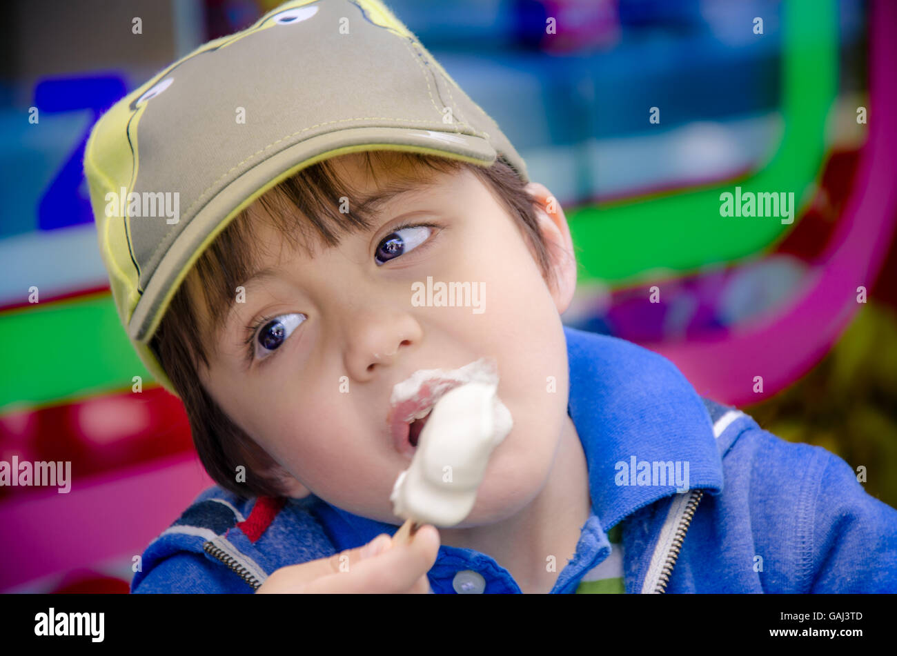 Un jeune garçon portant une casquette mange une glace sur un bâton Banque D'Images