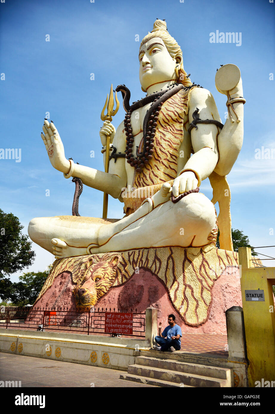 Un homme assis en bas de l'immense statue du dieu Shiva qui bénit bienvenue à tous les pèlerins visitant Nageshwar temple dans le Gujarat. Banque D'Images