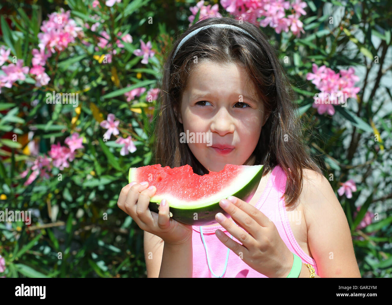 Jolie petite fille avec de longs cheveux bruns de manger une tranche de pastèque en été Banque D'Images