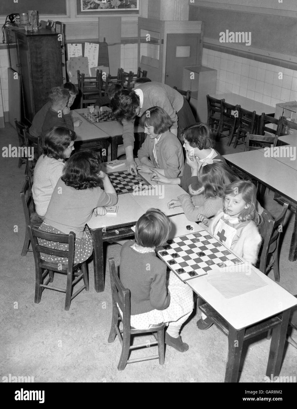 Les enfants jouant un jeu de draft sous la supervision d'un superviseur et certains garçons jouant un jeu d'échecs, à l'école primaire de Turnham. Banque D'Images
