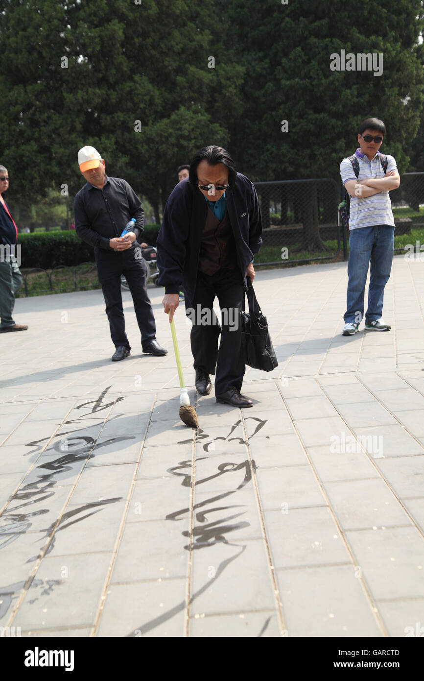 Un Chinois s'amuse à l'aide d'un pinceau et de l'eau énorme à peindre les caractères chinois sur le carrelage dans le parc du Temple du Ciel. Beijing, Chine. Banque D'Images