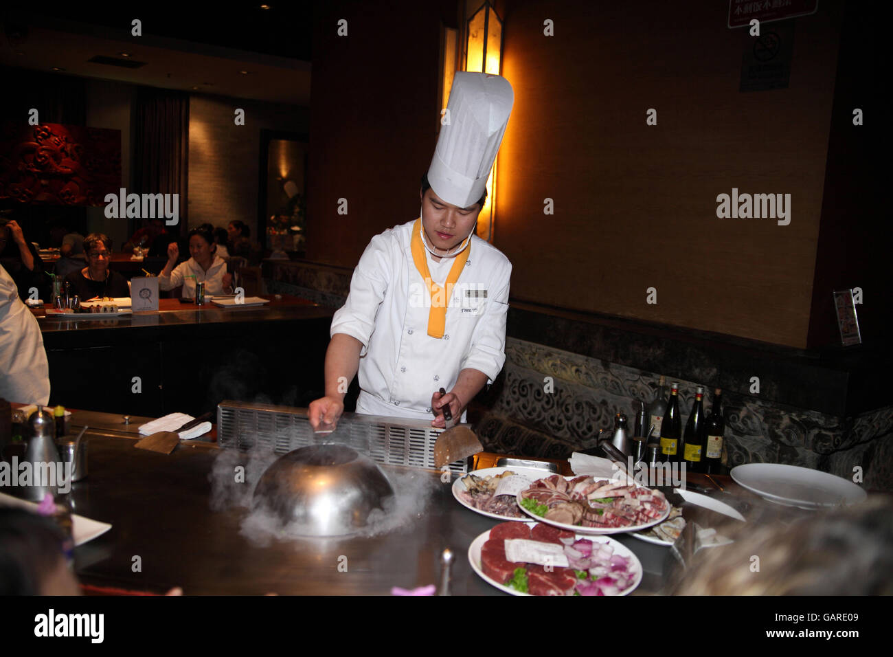 Un cuisinier chinois dans un restaurant chinois authentique portant uniforme blanc et un chapeau, met un couvercle métallique ronde sur la nourriture il est remuer la friture. Beijing, Chine. Banque D'Images