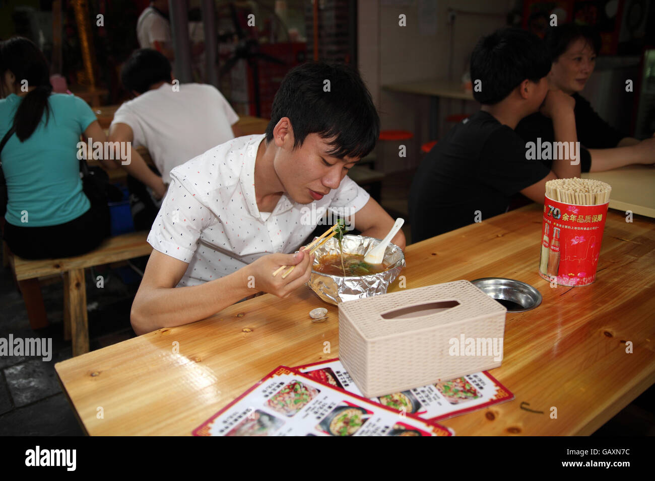 Jeune homme d'origine chinoise est en train de déjeuner dans un restaurant, il utilise des baguettes en mangeant de la soupe. Le marché de Guilin, Guangxi, Chine Banque D'Images