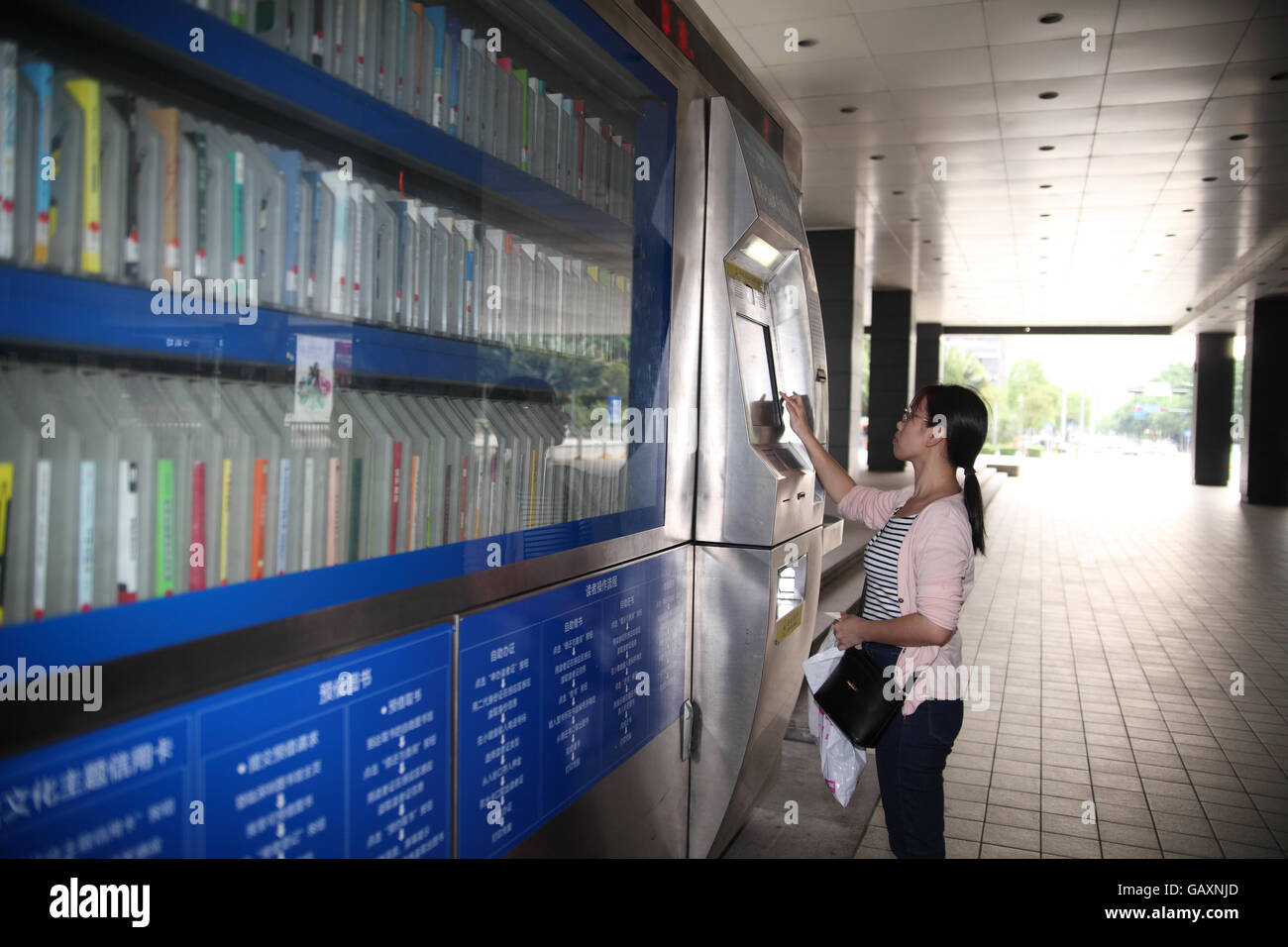 Une jeune femme à l'aide d'une machine libre-service automatique machine bibliothèque de louer ou d'emprunter un livre. Shenzhen, Chine Banque D'Images