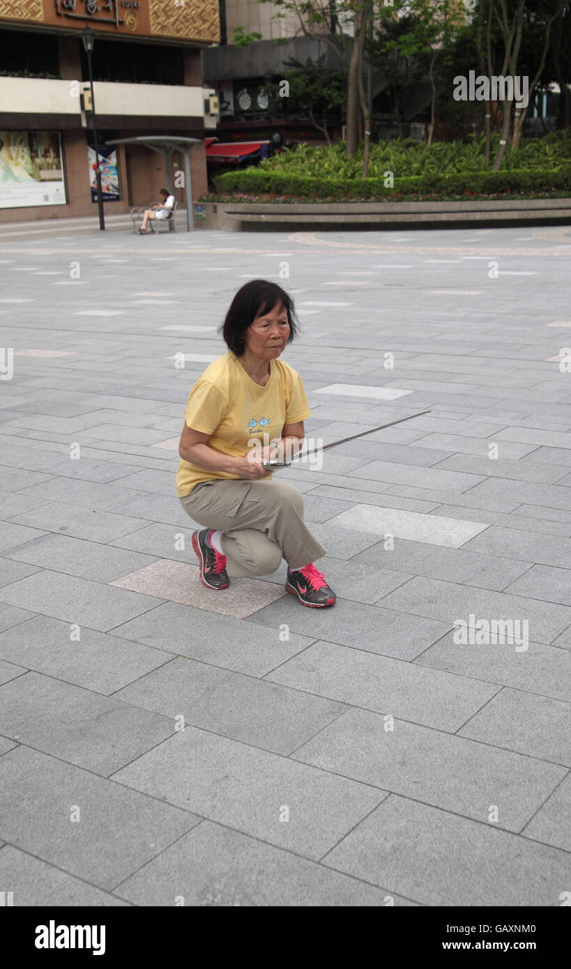 Une vieille femme chinoise à la retraite est très intense et se concentrer comme elle le fait le Tai Chi dans un parc public à l'aide d'une lance ou une épée. Kowloon, Hong Kong. Banque D'Images