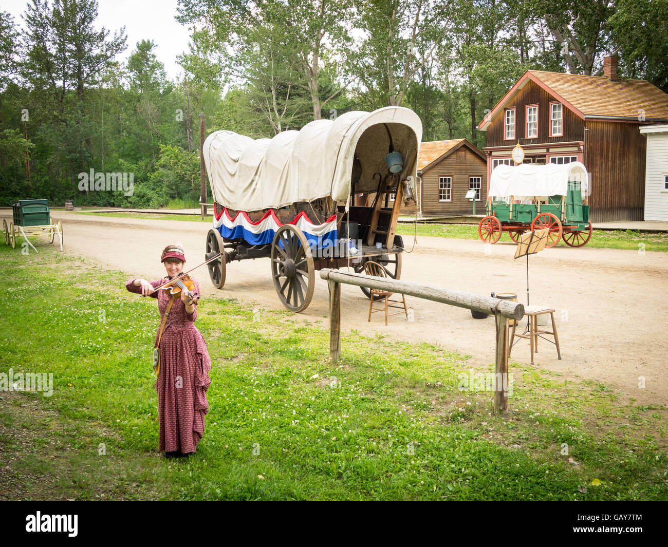 Un violoneux en costume joue en face d'un wagon couvert sur la rue '1885' au parc du Fort Edmonton à Edmonton, Canada. Banque D'Images