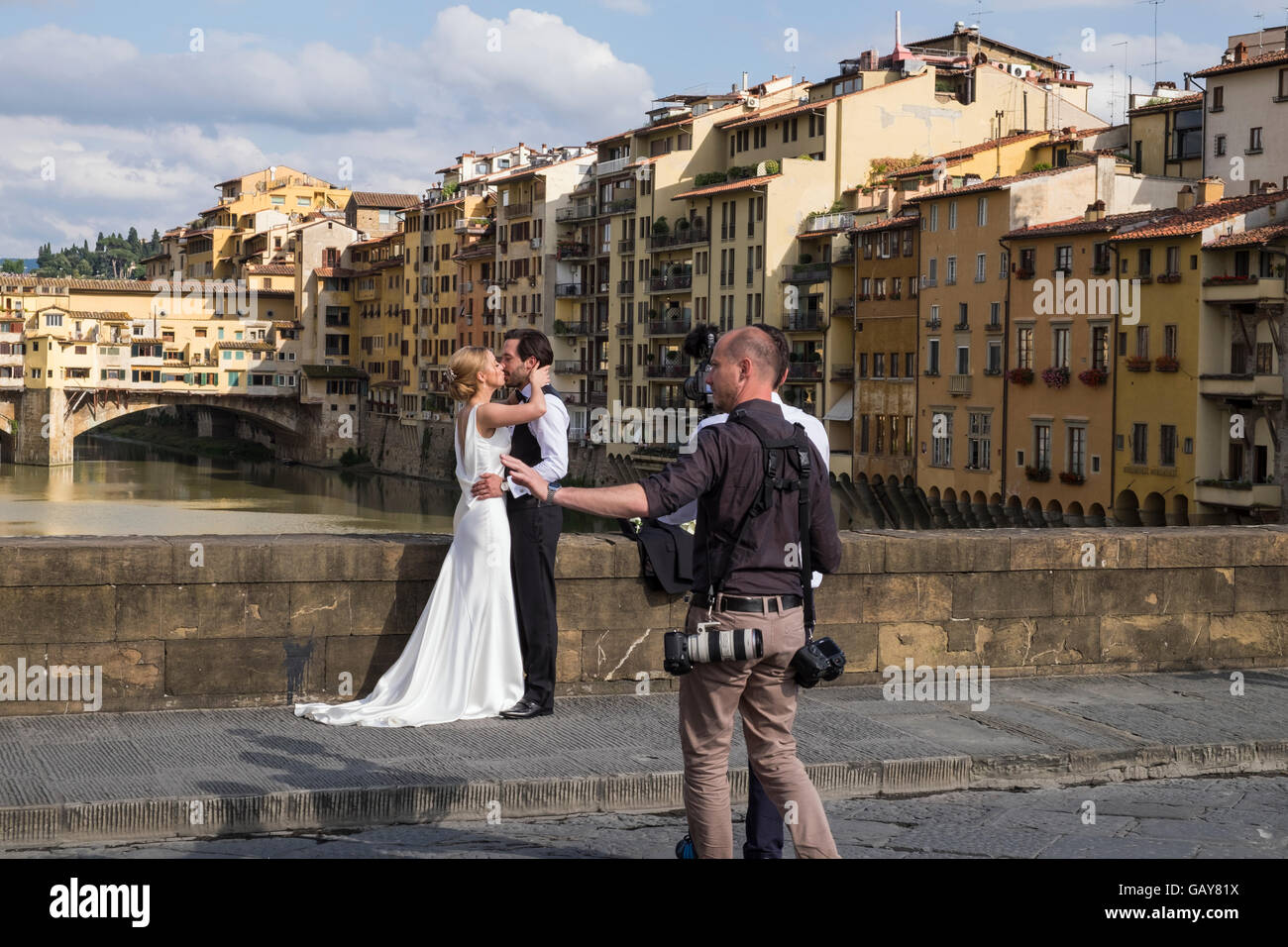 Wedding couple haveing leurs photos prises sur le Ponte Santa Trinita avec le Ponte Vecchio en arrière-plan, Florence, Toscane Banque D'Images