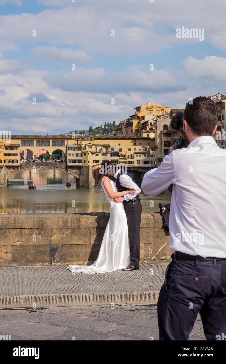 Wedding couple haveing leurs photos prises sur le Ponte Santa Trinita avec le Ponte Vecchio en arrière-plan, Florence, Toscane Banque D'Images