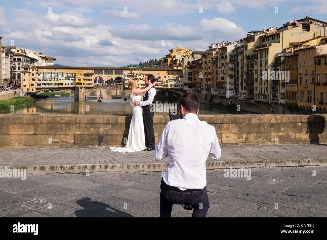 Wedding couple haveing leurs photos prises sur le Ponte Santa Trinita avec le Ponte Vecchio en arrière-plan, Florence, Toscane Banque D'Images