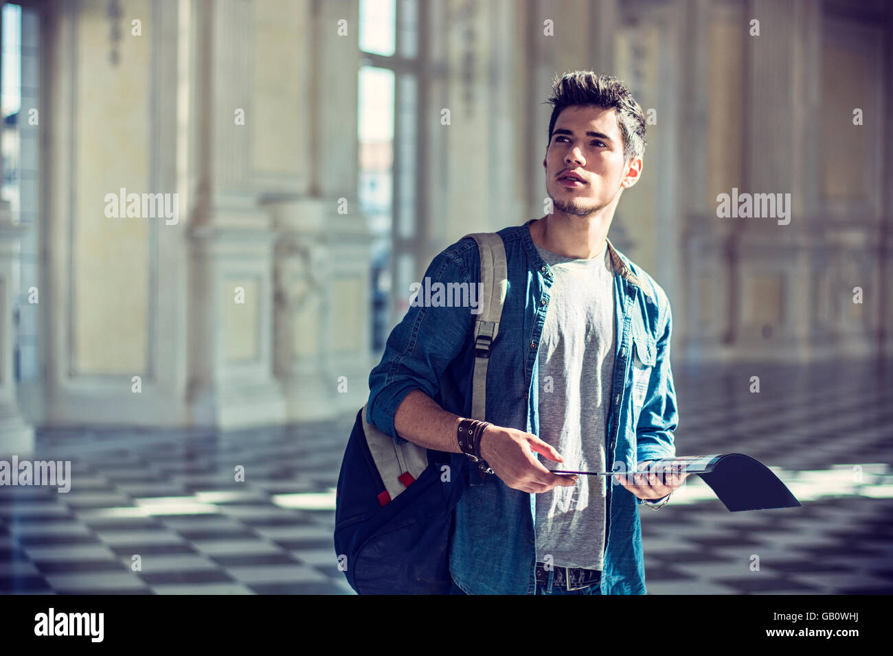 Moitié du corps d'un beau jeune homme pensif, tenant un guide, à la recherche à l'intérieur un musée Banque D'Images