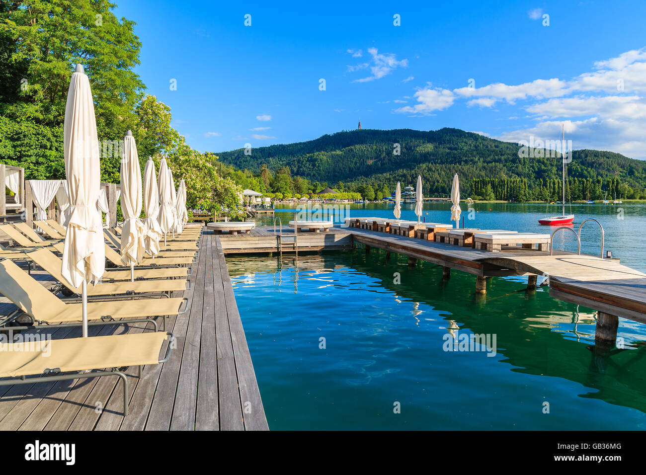 Chaises longues et lits sur terrasse en bois et vue sur beau lac alpin Worthersee en été, Autriche Banque D'Images