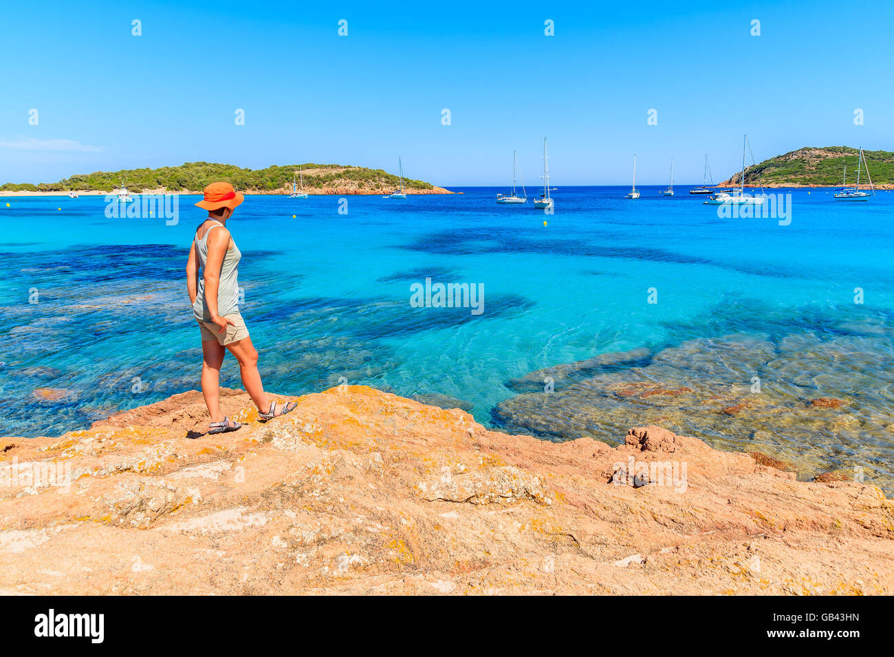 Jeune femme debout sur le roc et touristiques à l'eau de mer à l'azure de la baie de Santa giulia, Corse, France Banque D'Images