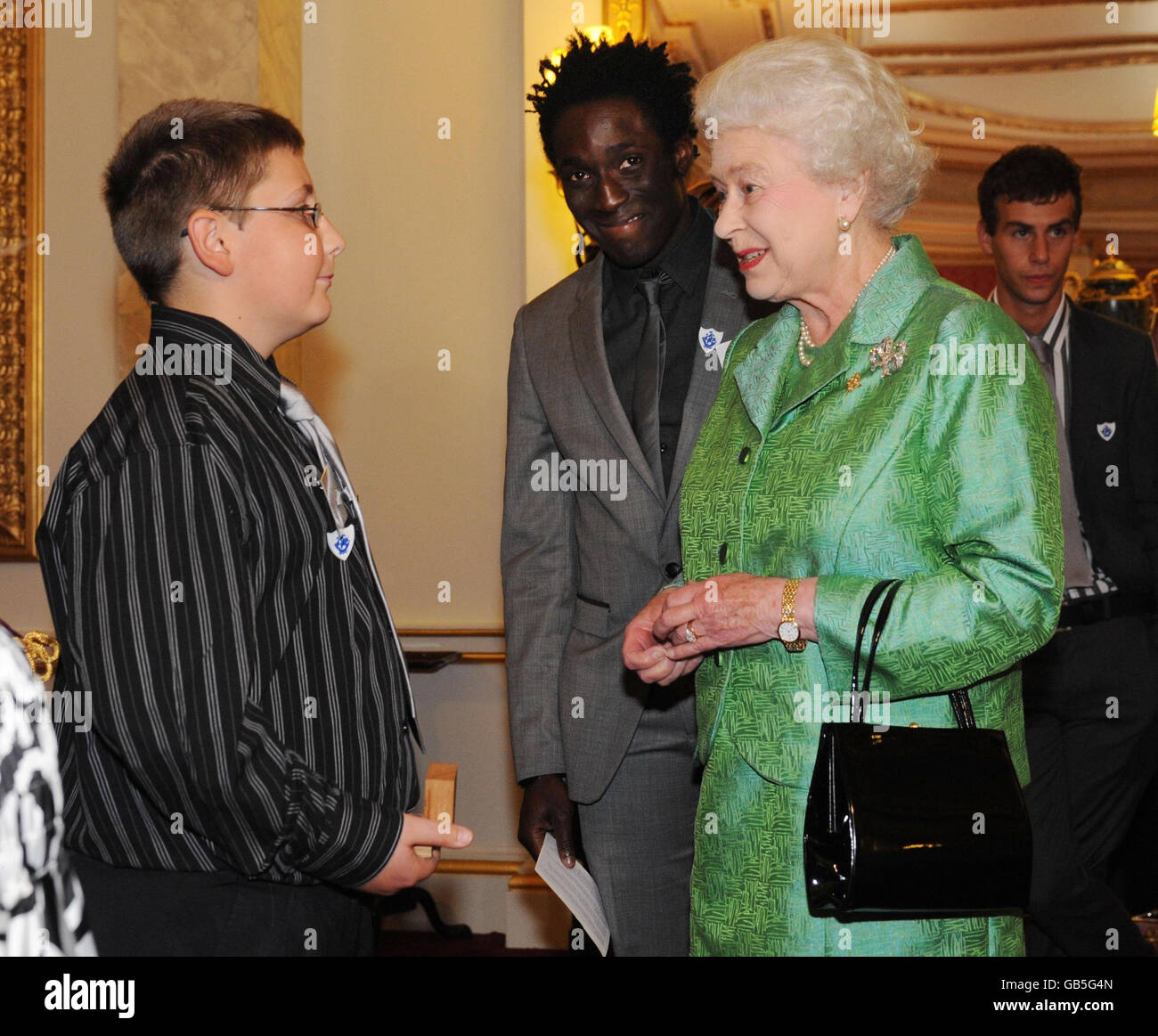 La reine Elizabeth II de Grande-Bretagne, accompagnée de l'actuel présentateur de Blue Peter Andy Akinwolere (au centre), présente un insigne de Blue Peter d'or à Iestyn Davies, 12 ans, du pays de Galles,L'OMS a élevé 26,000 personnes pour l'Ambulance aérienne galloise après avoir été secourue par eux suite à un accident grave, lors d'une réception pour marquer le 50e anniversaire du programme au Palais de Buckingham, Londres. Banque D'Images