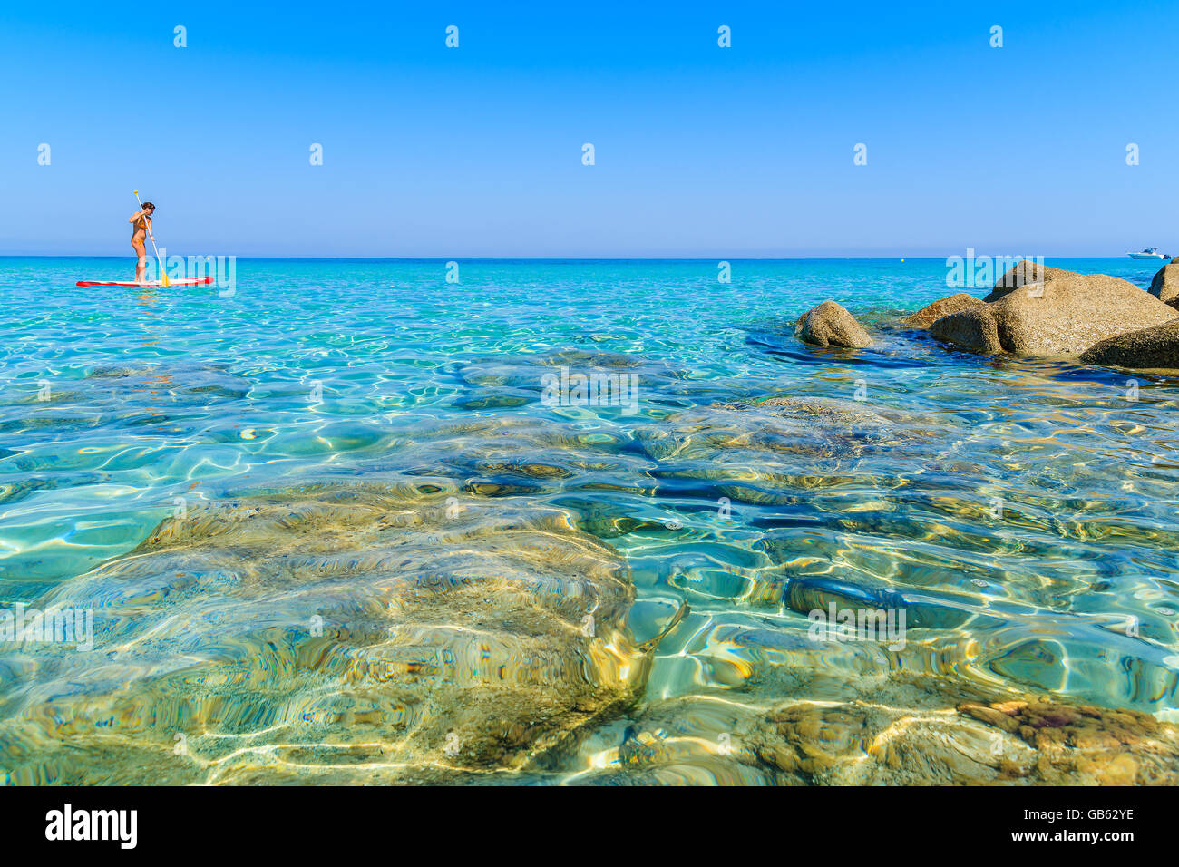 L'eau de mer cristalline et plage de Bodri femme non identifiée sur une planche de surf dans la distance, Corse, France Banque D'Images